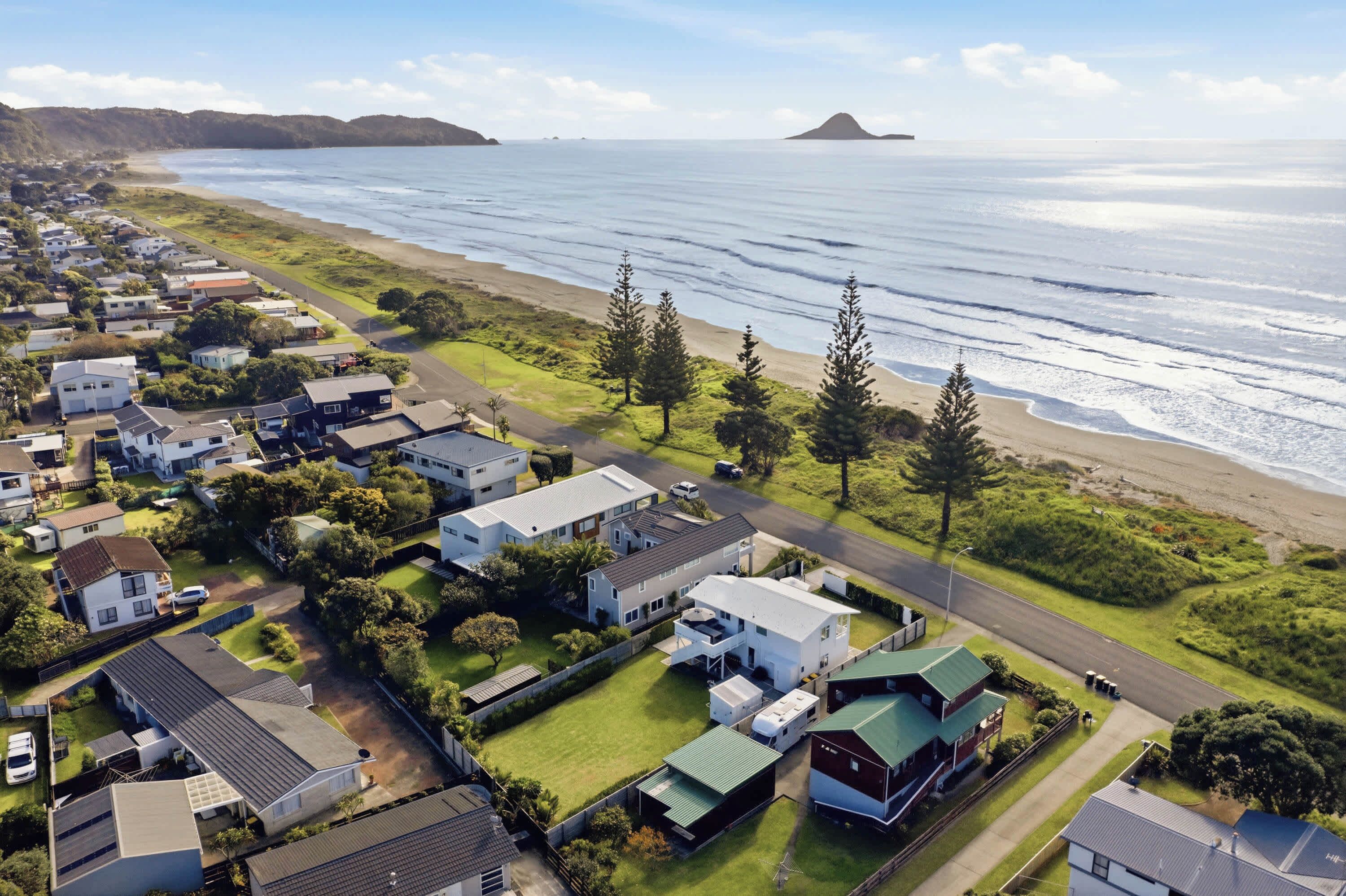 A coastal residential area with houses, a beach, and a mountain in the background.