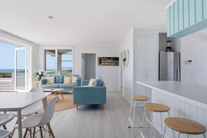 A modern kitchen with white cabinets, a stainless steel refrigerator, and a bar area with stools. - Ohope Beach Bliss Stunning Sea Views & Family fun (Ōhope)