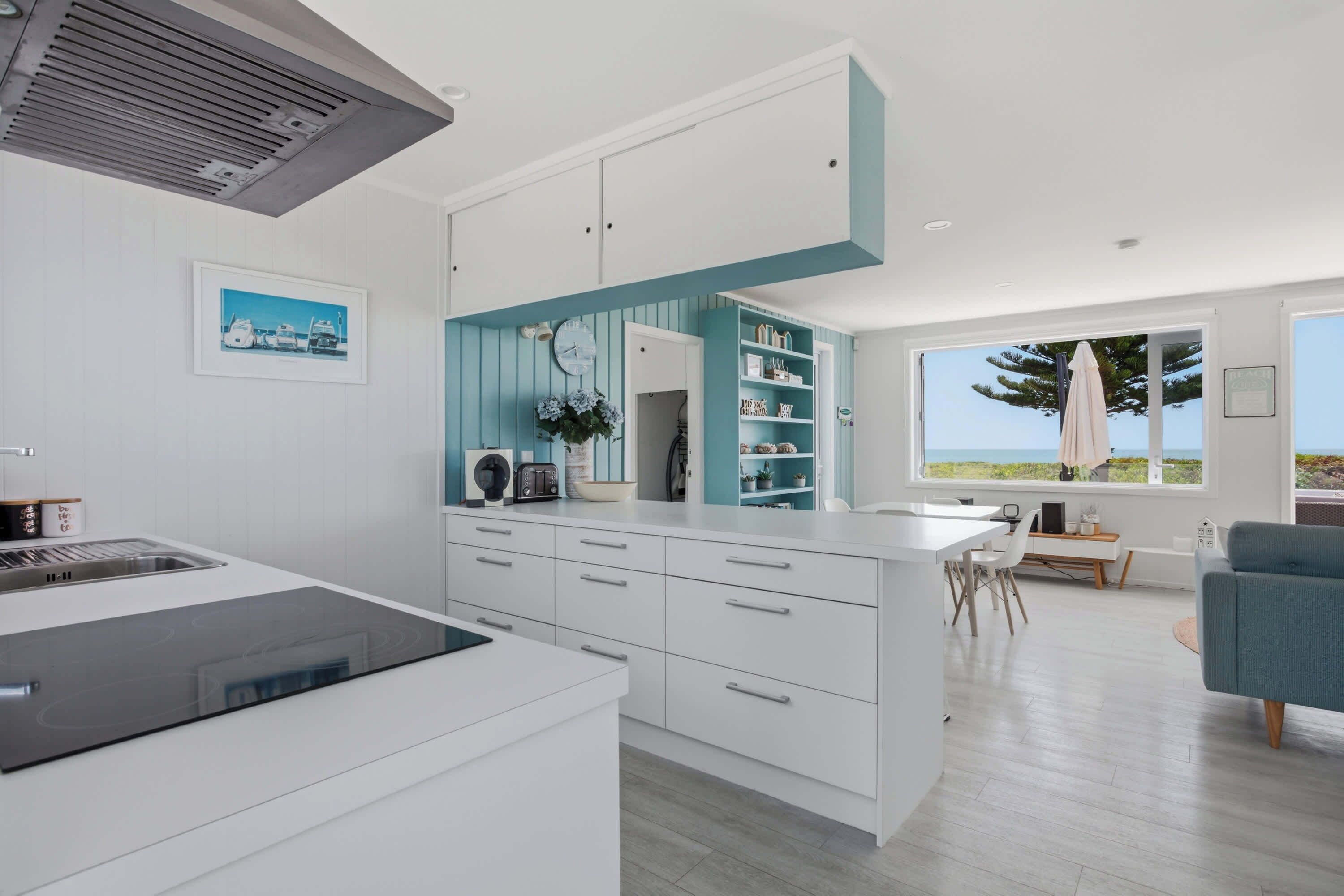 A modern kitchen with white cabinetry, a built-in island, and a view of the ocean through large windows.