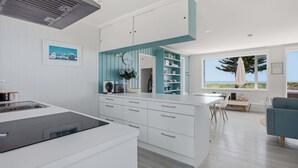 Una cucina moderna con mobili bianchi, un'isola integrata e vista sull'oceano attraverso ampie finestre.