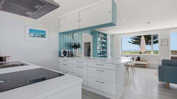A modern kitchen with white cabinetry, a built-in island, and a view of the ocean through large windows.