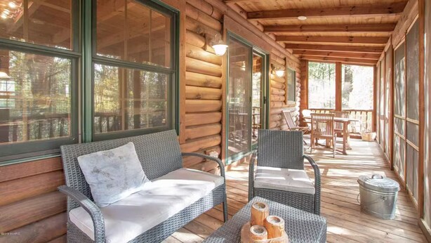 Eine Holzhütte mit überdachter Veranda, Korbmöbeln und großen Fenstern.