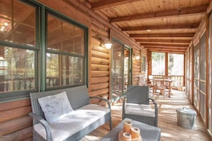 Una cabaña de madera con un porche cubierto, muebles de mimbre y ventanas amplias.
