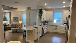 A modern kitchen with white cabinetry, a central island, and a dining area with a round table and chairs. - Brand New Naples Villa in a Resort Style gated community! (Naples)