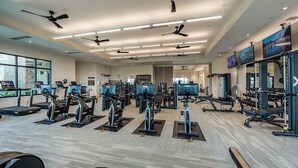 A modern gym with multiple exercise machines, ceiling fans, and large windows. - Brand New Naples Villa in a Resort Style gated community! (Naples)