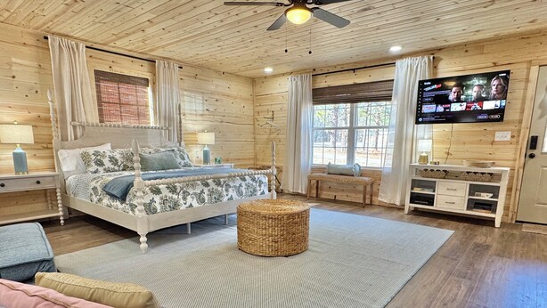 Acogedora habitación de cabaña de madera con cama, televisión, banco y mueble para televisión.
