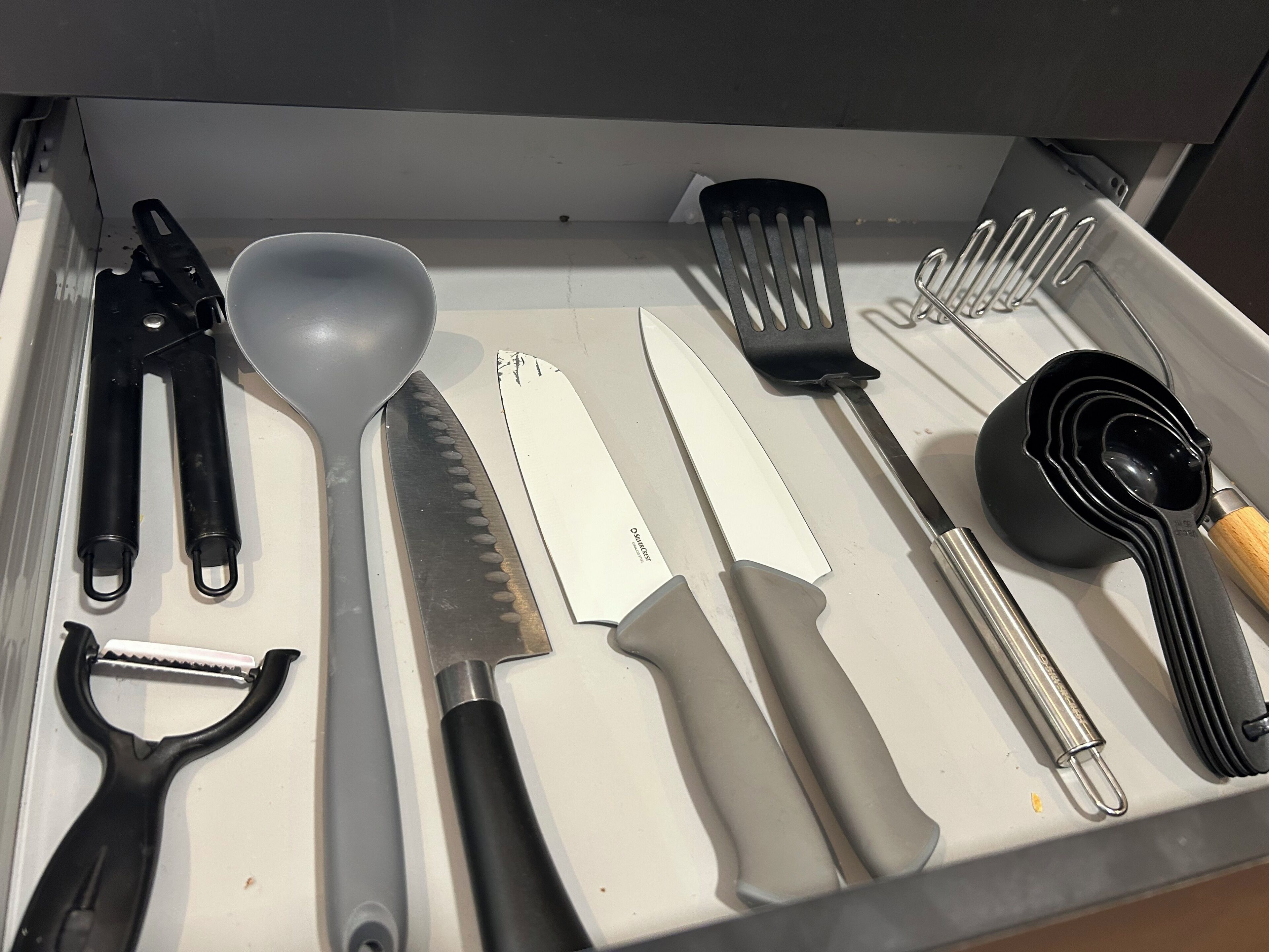 A drawer containing various kitchen utensils including a spatula, knife, and spoon.