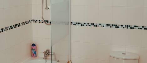 Un baño con una bañera blanca, cabina de ducha de cristal, inodoro y una alfombra pequeña.