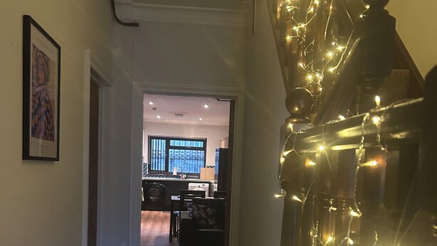 A hallway with a staircase leading to a living area. There is a framed picture on the wall and a string of lights on the staircase. - The Phoenix  (Swansea)