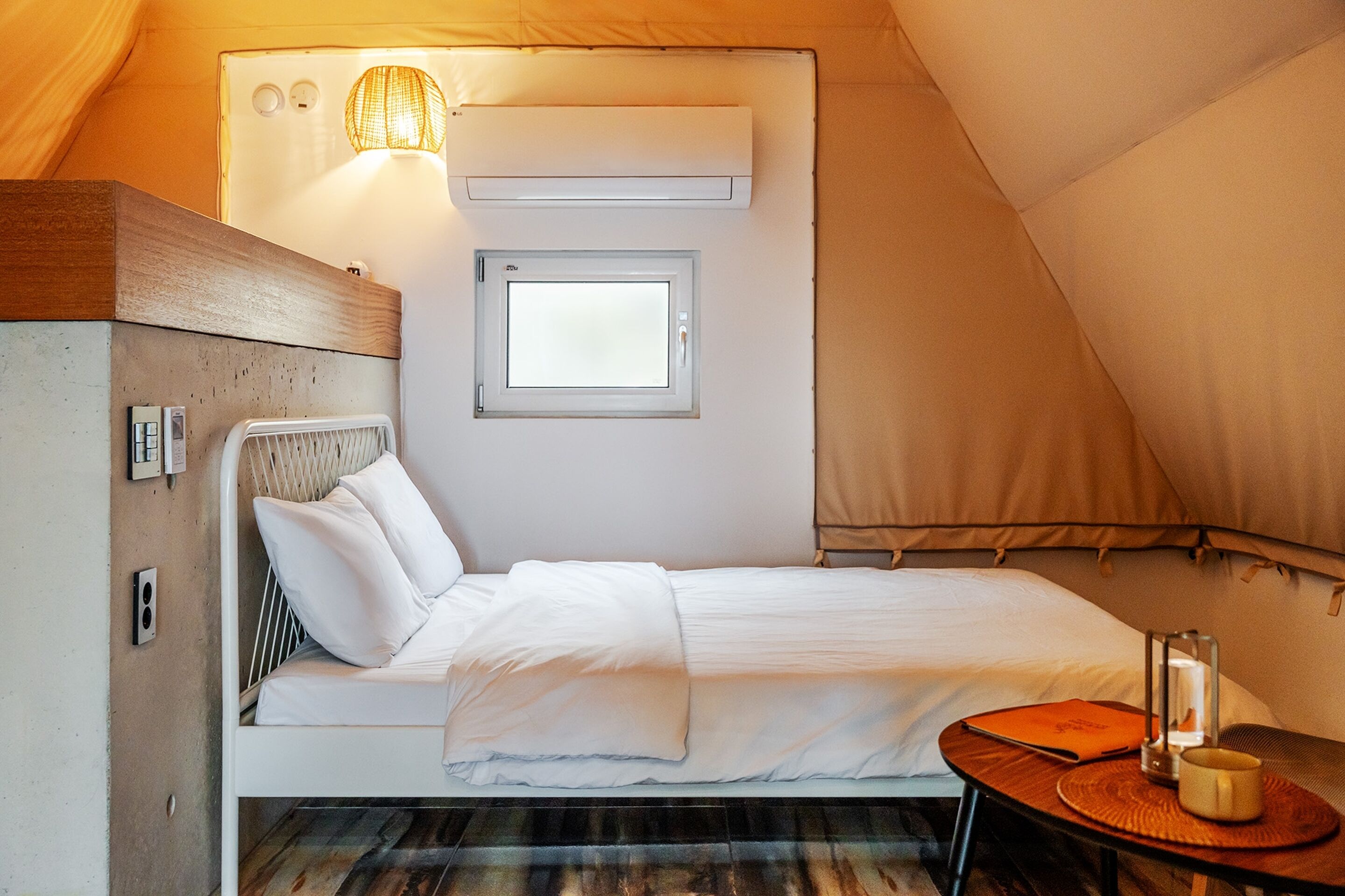 A cozy tented room with a bed, a small table, a lamp, and a window.
