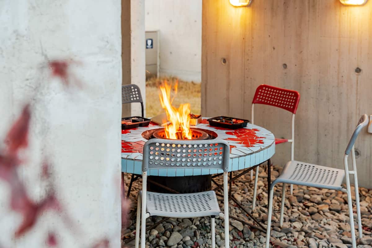 Ein runder Tisch mit Feuerstelle in der Mitte, umgeben von Metallstühlen.