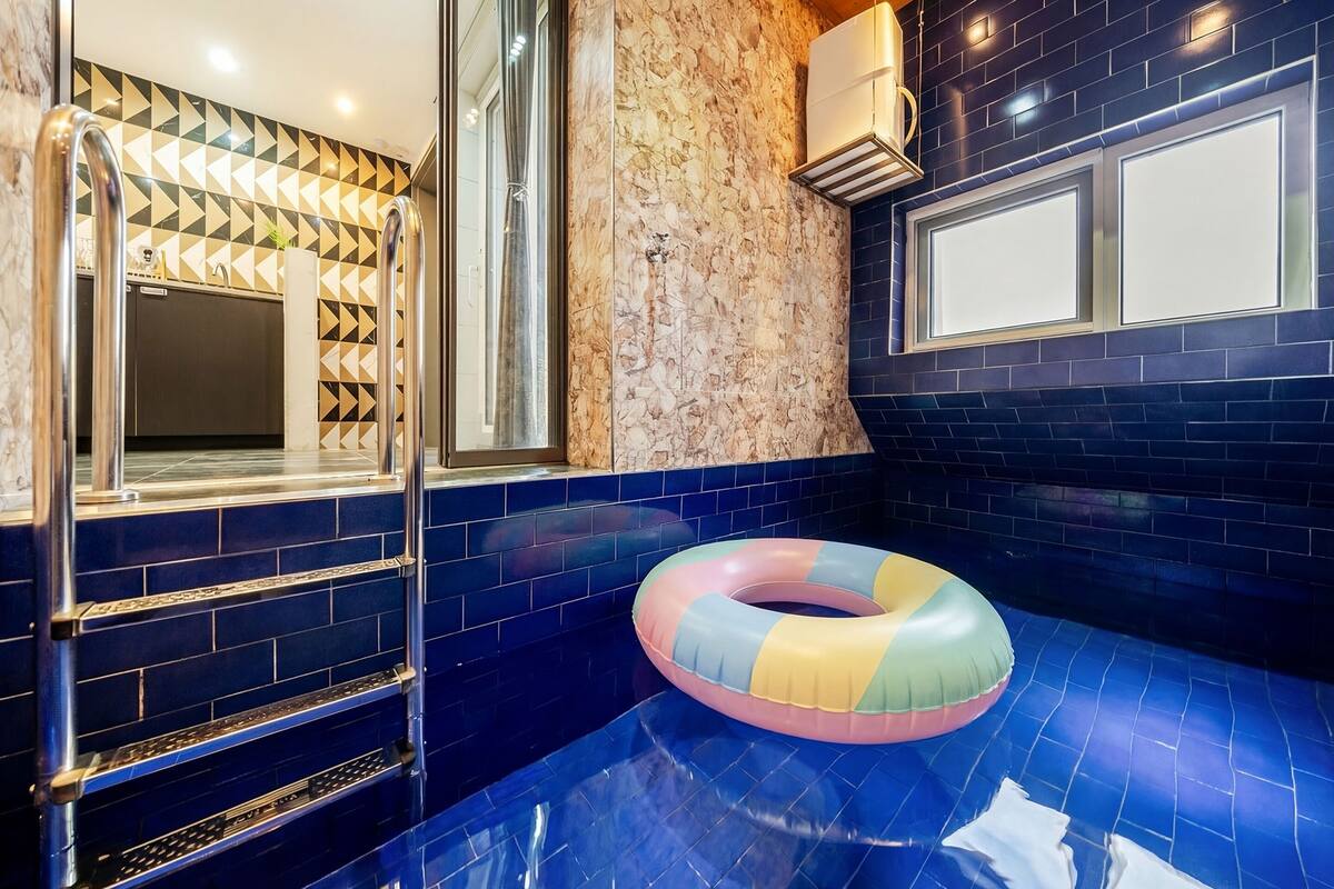 Ein Badezimmer mit blau gefliestem Boden, einem bunten Schwimmreifen und einem Spiegel an einer Wand mit geometrischem Muster.