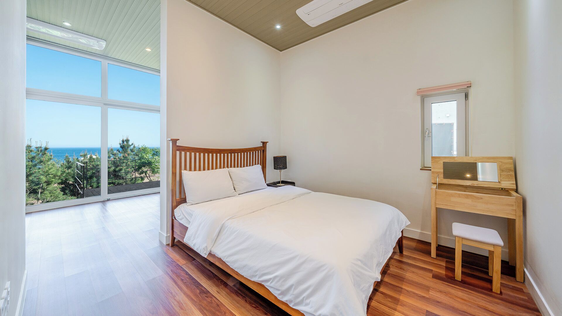 Een slaapkamer met een bed, nachtkastje, spiegel en uitzicht op zee.