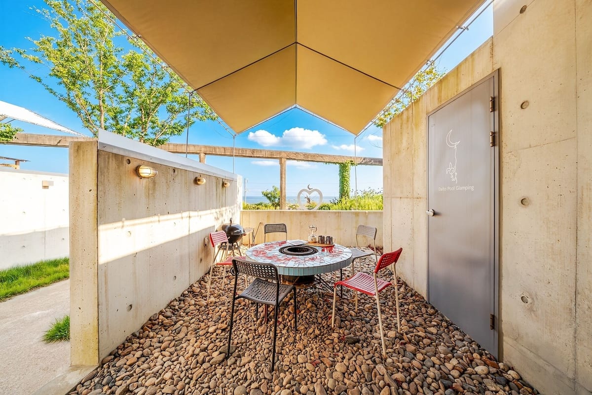 Ein überdachter Außenbereich mit Tisch, Stühlen, einem Grill und Blick auf das Meer.