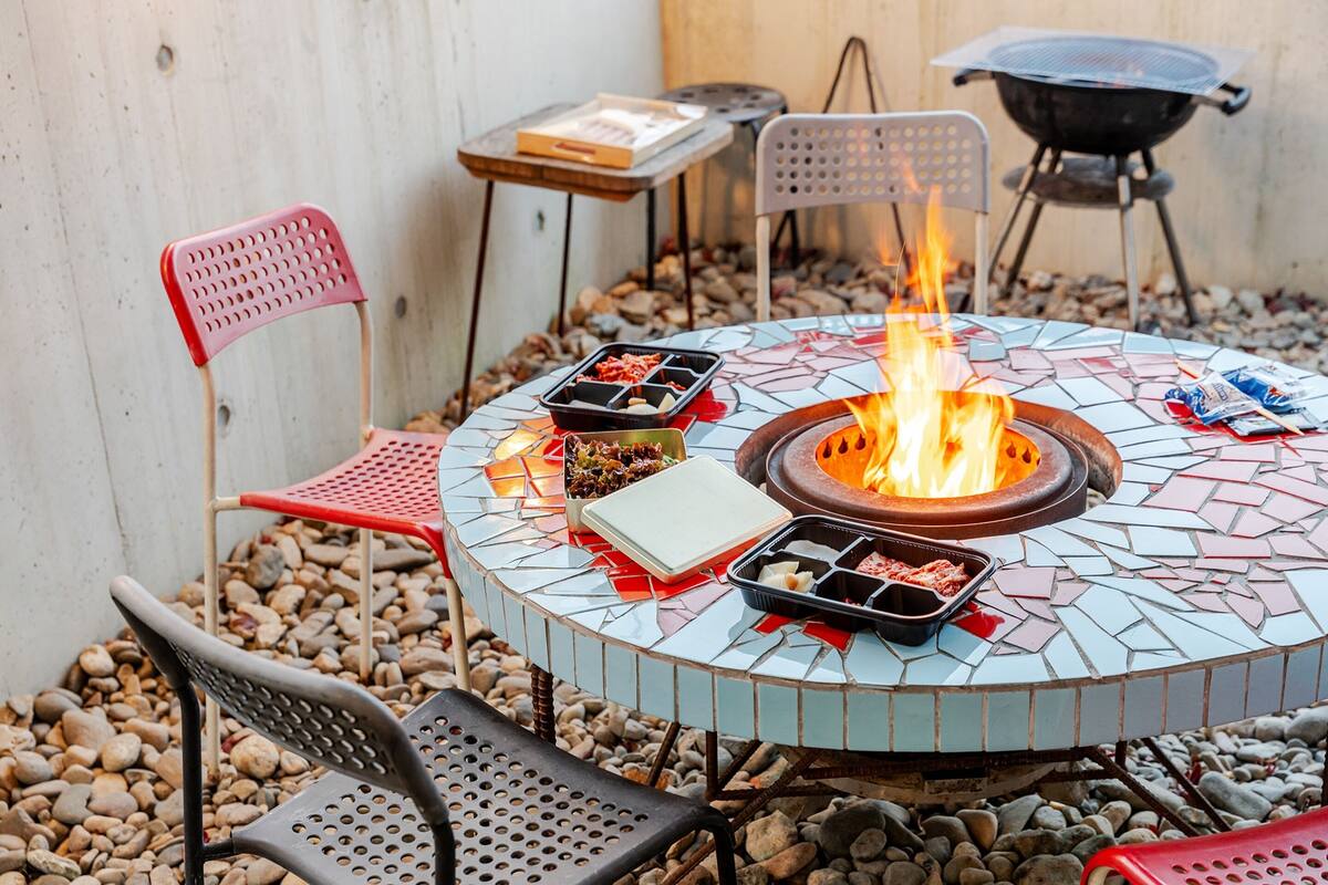 Ein rundes Feuerbecken im Freien mit Mosaikfliesenmuster, umgeben von Sitzgelegenheiten und einem Grill.