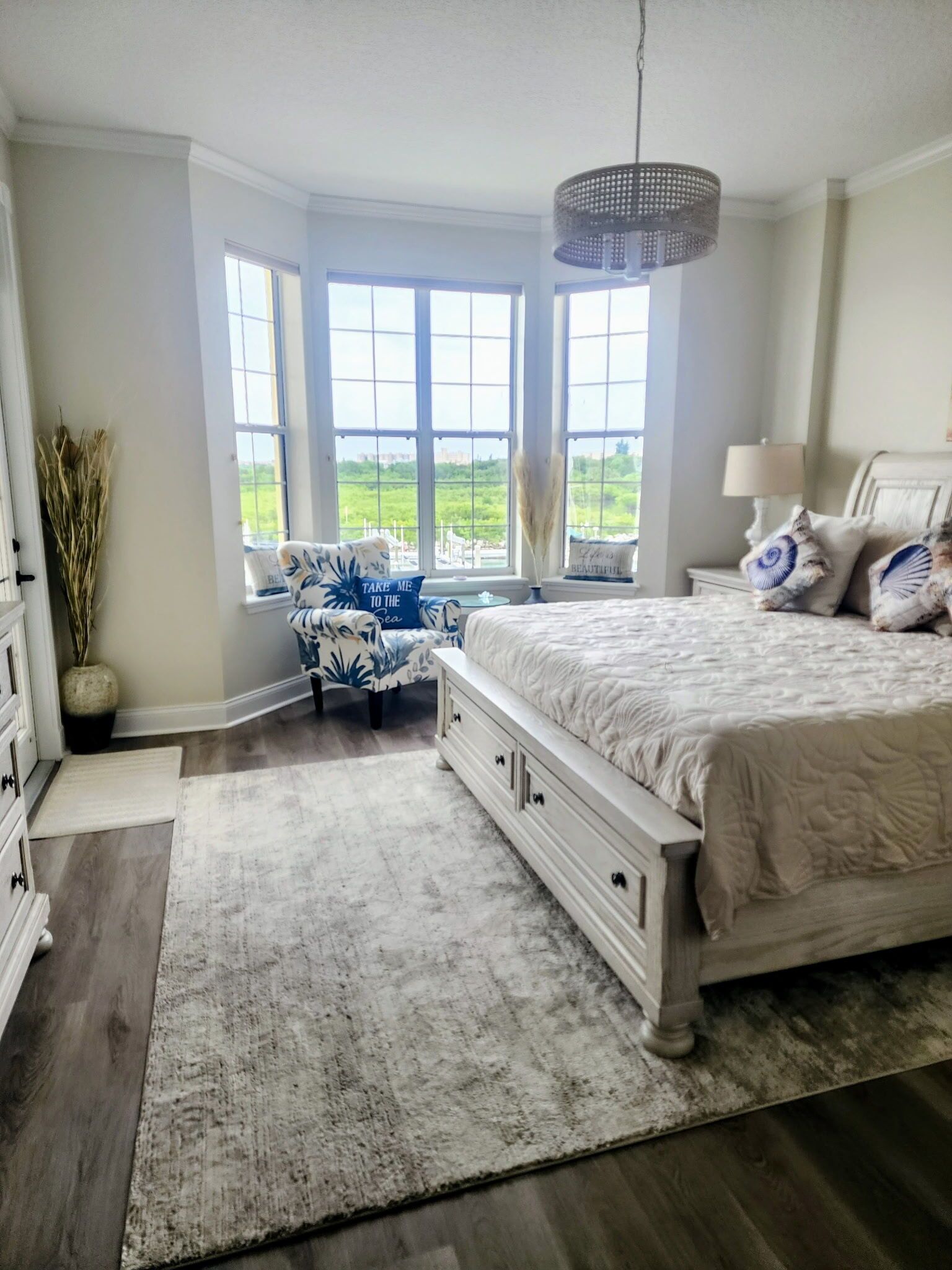 A bedroom with a large bed, a window with a view, a dresser, and a lamp.