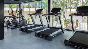 Ein Fitnessstudio mit Laufbändern, Crosstrainern und Kurzhanteln, ausgestattet mit großen Fenstern und einem Betonboden.