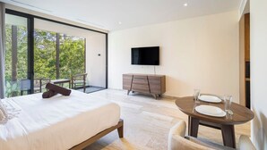 A modern bedroom with a large bed, a TV mounted on the wall, a wooden dresser, and a balcony with a view of trees. - Pool-View Studio Retreat | Wi-Fi, Smart TV and AC (Tulum)