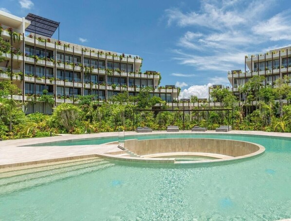 Een modern hotel met een centraal gelegen zwembad, omringd door weelderige begroeiing en meerdere balkons met planten.