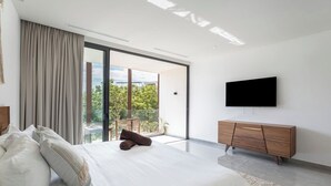 A modern bedroom with a large bed, a wooden dresser, a flat-screen TV, and a balcony with a view of greenery. - Summer getaway! Studio with gym and 6 rooftop pool (Tulum)