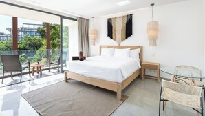 A modern bedroom with a large bed, a glass table, wicker chairs, and a balcony with a view of greenery. - Magnificent studio with pool views, gym and roftop (Tulum)