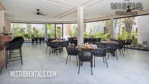 A spacious outdoor dining area with multiple tables and chairs, surrounded by large windows offering views of greenery. - Magnificent studio with pool views, gym and roftop (Tulum)