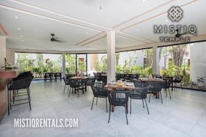 A spacious outdoor dining area with multiple tables and chairs, surrounded by large windows offering views of greenery. - Magnificent studio with pool views, gym and roftop (Tulum)