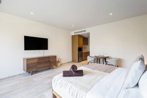 Et moderne hotelværelse med seng, fjernsyn, et lille køkken og spiseplads.