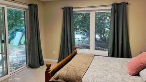 Un dormitorio con cama, ventana con cortinas, vista a un tobogán y puerta que da al exterior.