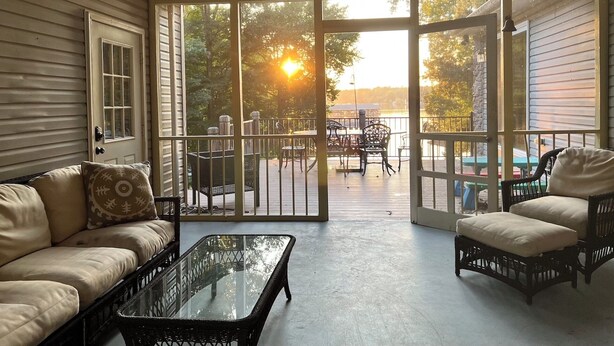 Un patio iluminado por el sol con un ventanal de vidrio que da a una terraza, amoblado con un sofá, sillas y una mesa.