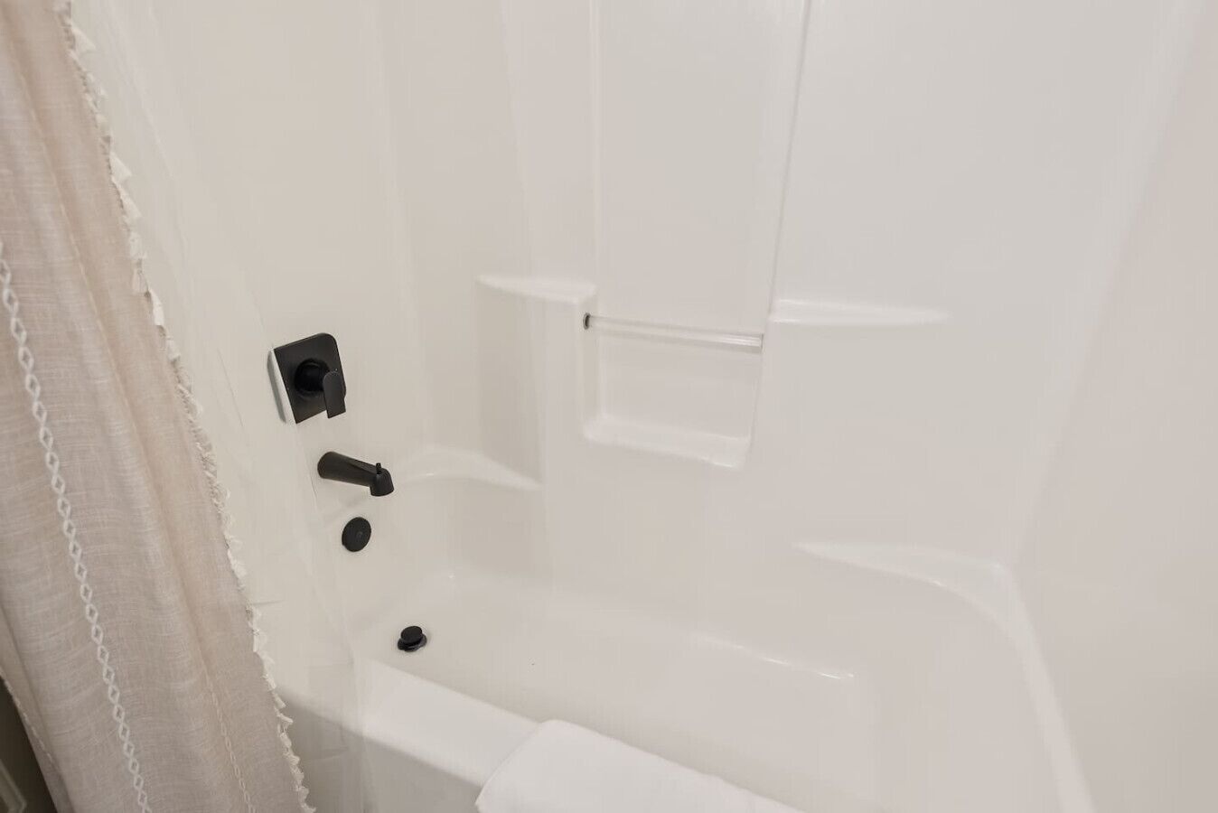 A white bathroom with a bathtub, a towel rack, and a shower curtain.