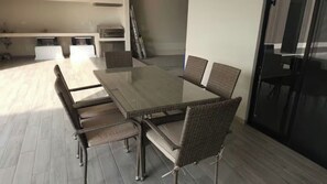 A dining area with a glass-top table and wicker chairs, a kitchen in the background, and a sliding glass door leading to an outdoor area.