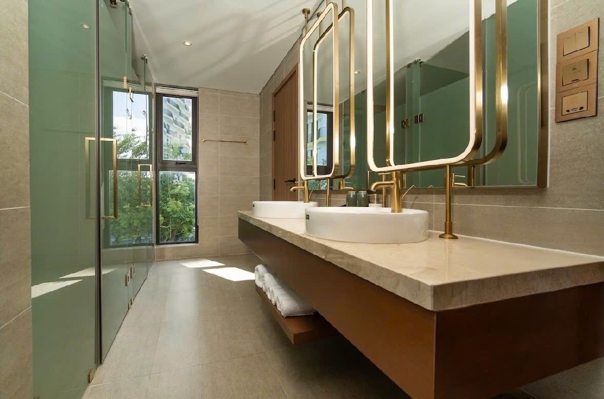 A modern bathroom with a glass shower enclosure, a vanity with two sinks, and a large mirror with gold frames.