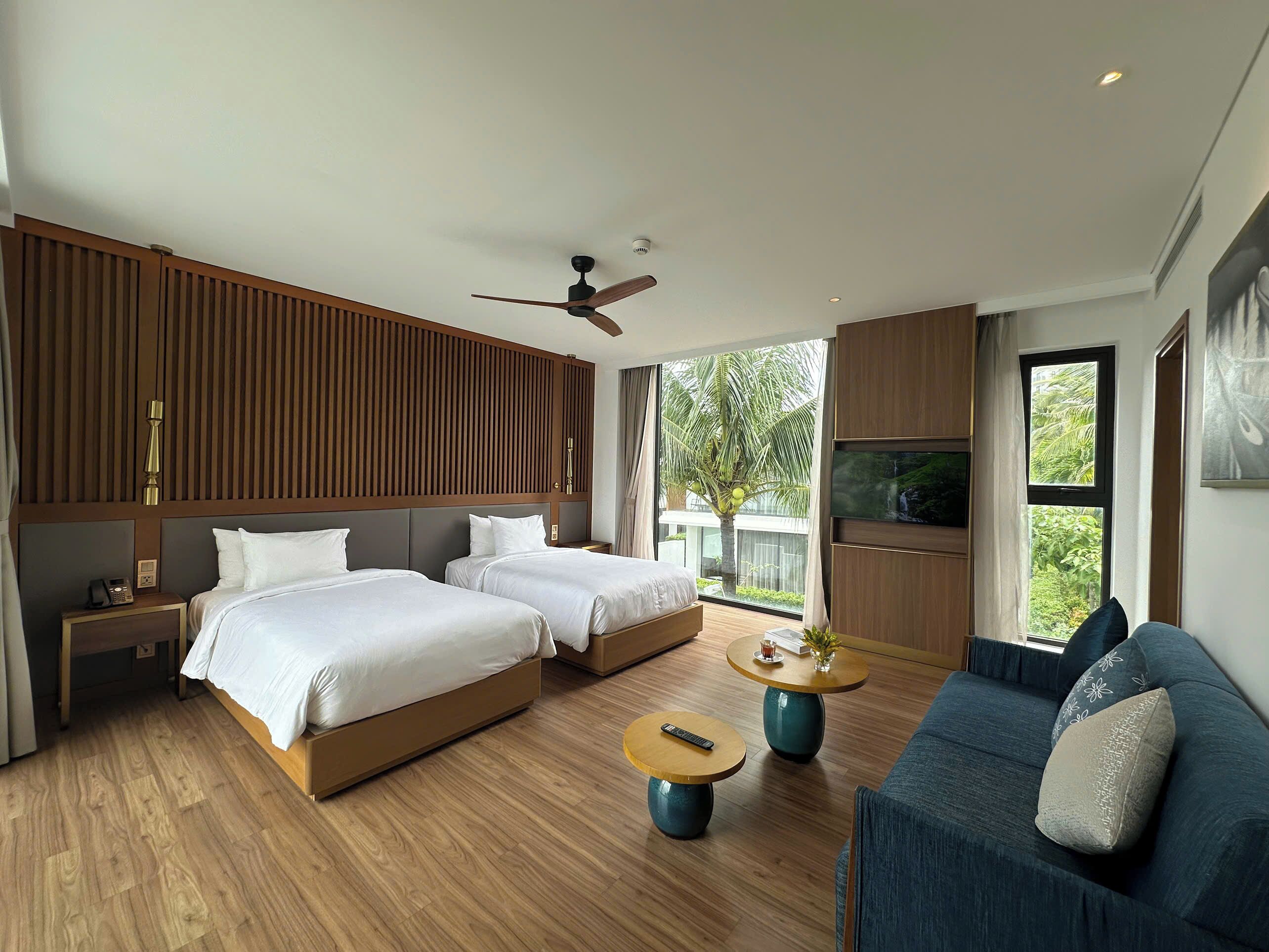 A modern hotel room with two beds, a sofa, a coffee table, and a TV.