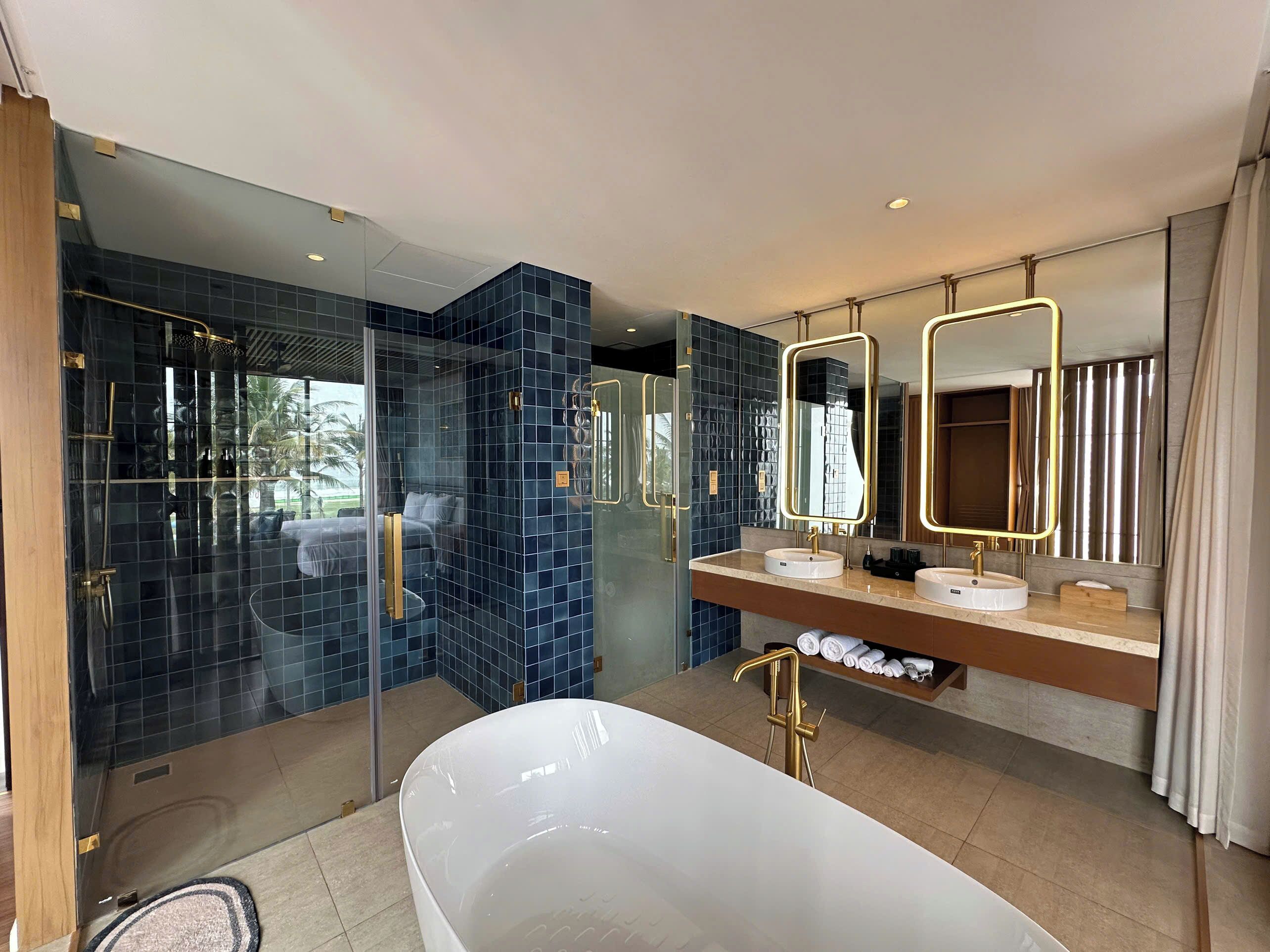 A modern bathroom with a glass-enclosed shower, a freestanding bathtub, and dual sinks with gold fixtures.