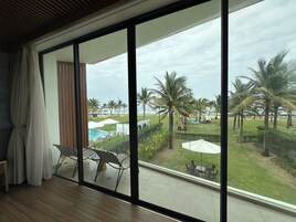 Una habitación con un gran ventanal corredera que da a una zona de piscina con sillas de descanso y sombrillas.