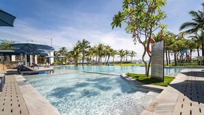 A swimming pool with clear water, surrounded by palm trees and lounge chairs.