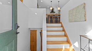 Eine Treppe mit Holzbalken führt zu einem Küchenbereich mit Holzsitzen und Pendelleuchten.
