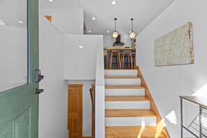 A staircase with wooden steps leading to a kitchen area with wooden stools and pendant lights. - Centrally Located, Renovated 4BR Stowe Getaway! (Stowe)