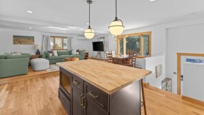 Eine moderne Küche mit einer Holztheke, einem Essbereich mit Tisch und Stühlen sowie ein Wohnzimmer mit einer Couch und einem Fernseher.