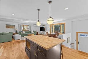A modern kitchen with a wooden island, a dining area with a table and chairs, and a living room with a sofa and a TV. - Centrally Located, Renovated 4BR Stowe Getaway! (Stowe)