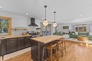 A modern kitchen with dark cabinets, a wooden island, and pendant lighting. - Centrally Located, Renovated 4BR Stowe Getaway! (Stowe)