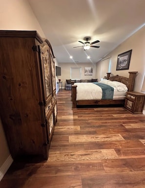 A bedroom with a large wooden wardrobe, a bed with a white comforter, a ceiling fan, and a wooden floor.