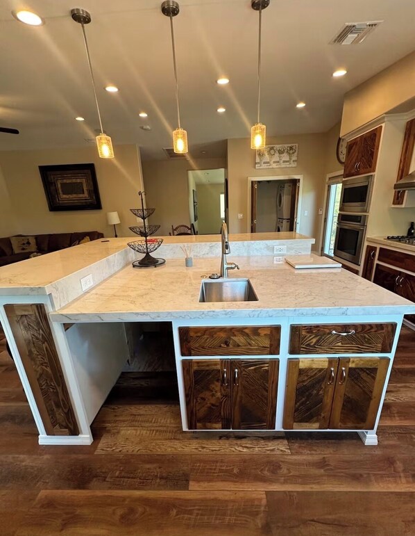 A spacious kitchen with a large island, wooden cabinets, and pendant lighting.