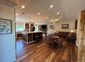 A spacious living area with a wooden floor, a dining table with chairs, a sofa, and a TV mounted on the wall.