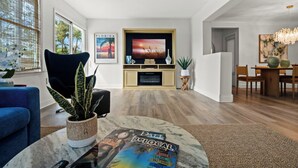 A modern living room with a television, a dining area, and a large window with blinds. - Coastal Retreat w/ Heated Pool & Games (Largo)