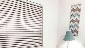 A bedroom with a bed, a nightstand, a lamp, a window with blinds, and a decorative wall piece.