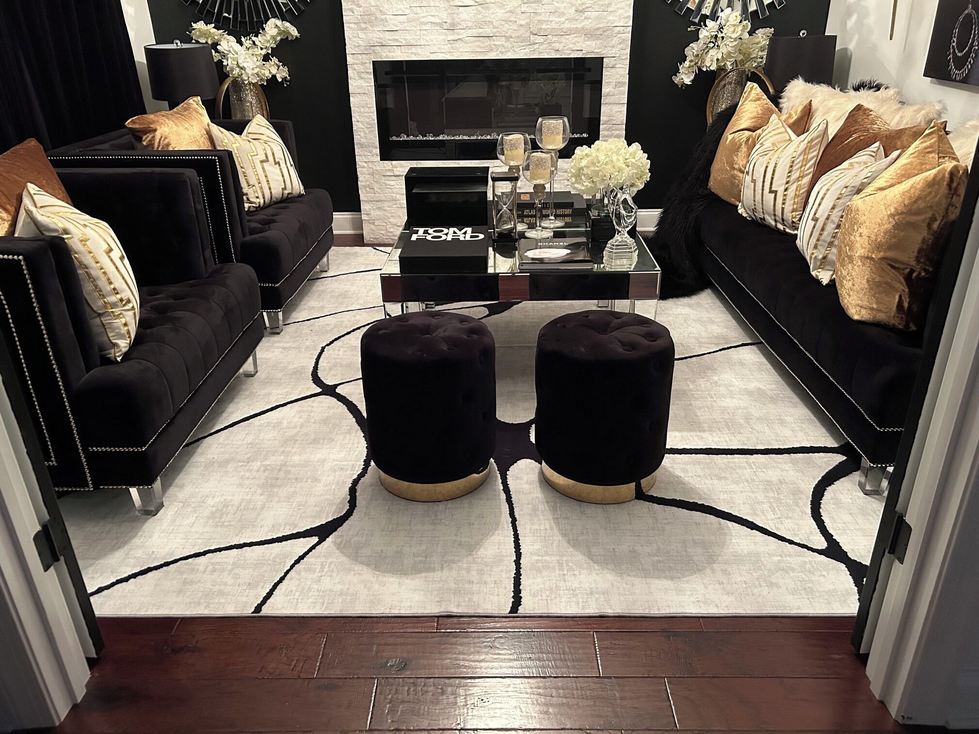 A modern living room with a black sofa, ottomans, a coffee table, and a fireplace.
