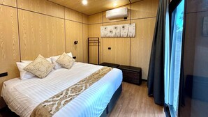 Ett hotellrum med ett träpanelat tak, en stor säng med mönstrade kuddar, en väggmonterad luftkonditioneringsanläggning och ett fönster med gardiner.