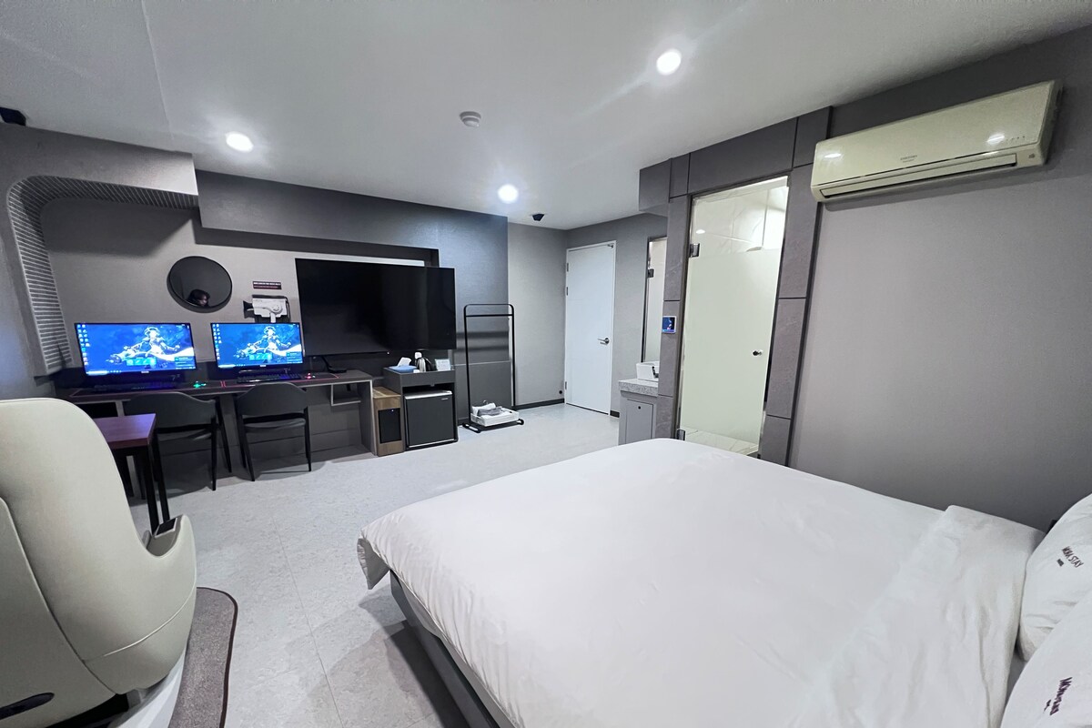 A hotel room with a bed, two desks with computers, a TV, and a wardrobe.